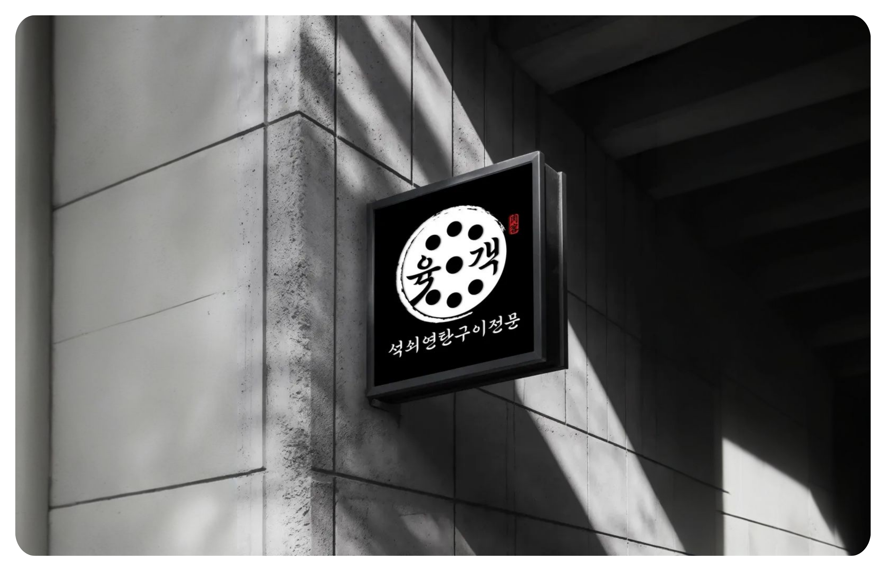 회색 건물 벽면에 검은색 간판이 걸려 있고, 간판에는 흰색 원형 로고와 한글 글자가 보인다.